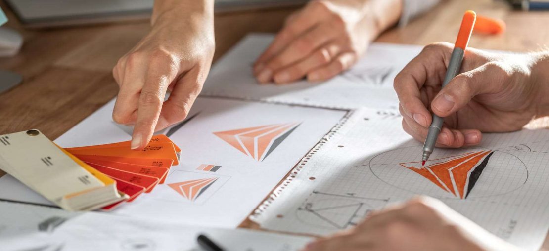 foto de dois pares de mãos desenhando no papel e criando logotipos e identidades visuais