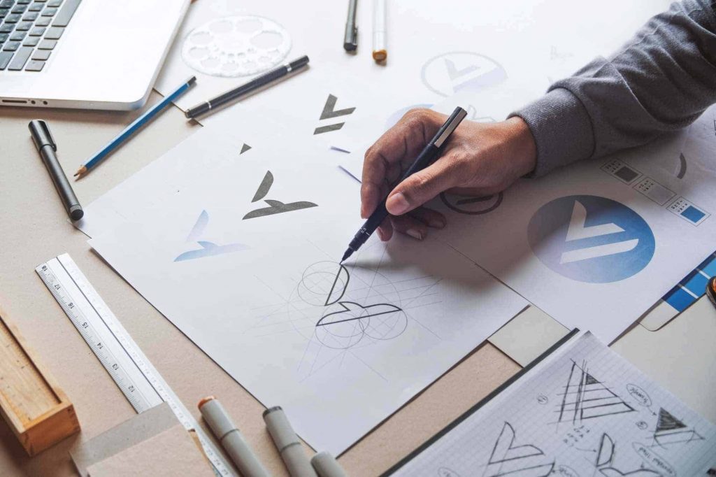 imagem mão com lápis, criado identidade visual de marca no papel- fuja dos logotipos grátis